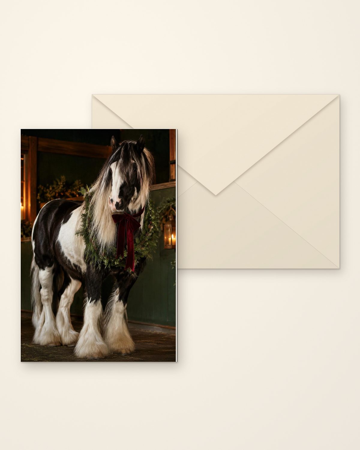 Front view of a single folded Christmas card showing a piebald cob wearing a wreath, standing in front of a cream envelope
